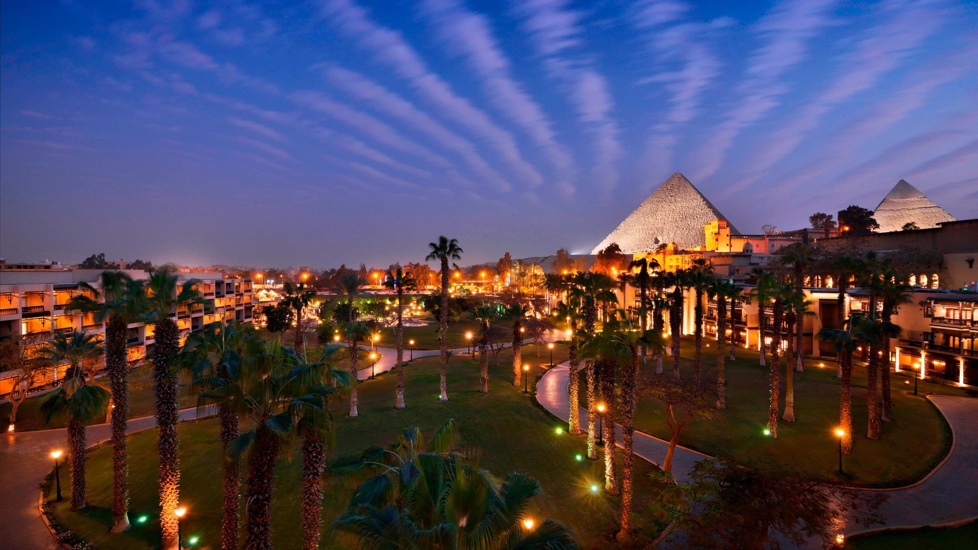 The gardens of Marriott Mena House at dusk, with the floodlit Great Pyramid beyond
